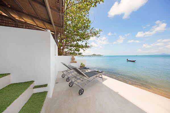 A poolside area with a lounge chair and a small table, a clear view of the sea, and a boat in the distance. - Hacienda Fisherman's Village Koh Samui (Koh Samui)