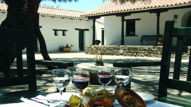 An outdoor dining area with a table set for two, featuring a bowl of bread, a basket of bread, and a plate of food. - Hacienda de Molinos (Molinos)