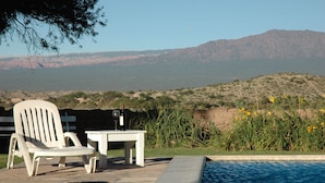 A poolside area with a chair and table, a view of a desert landscape, and a mountain range in the background. - Hacienda de Molinos (Molinos)