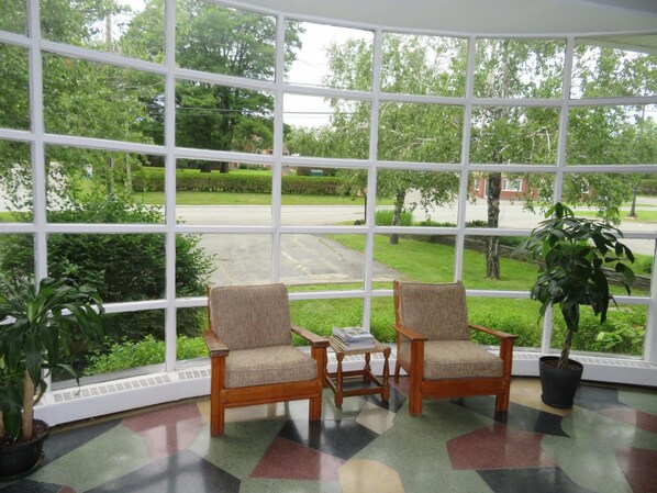 A room with two wooden chairs and a small table, large windows with a view of a green landscape and a road. - Motel La Paysanne (Sherbrooke)