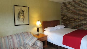 A hotel room with a bed, a nightstand with a lamp, a sofa, and a brick-patterned wall.