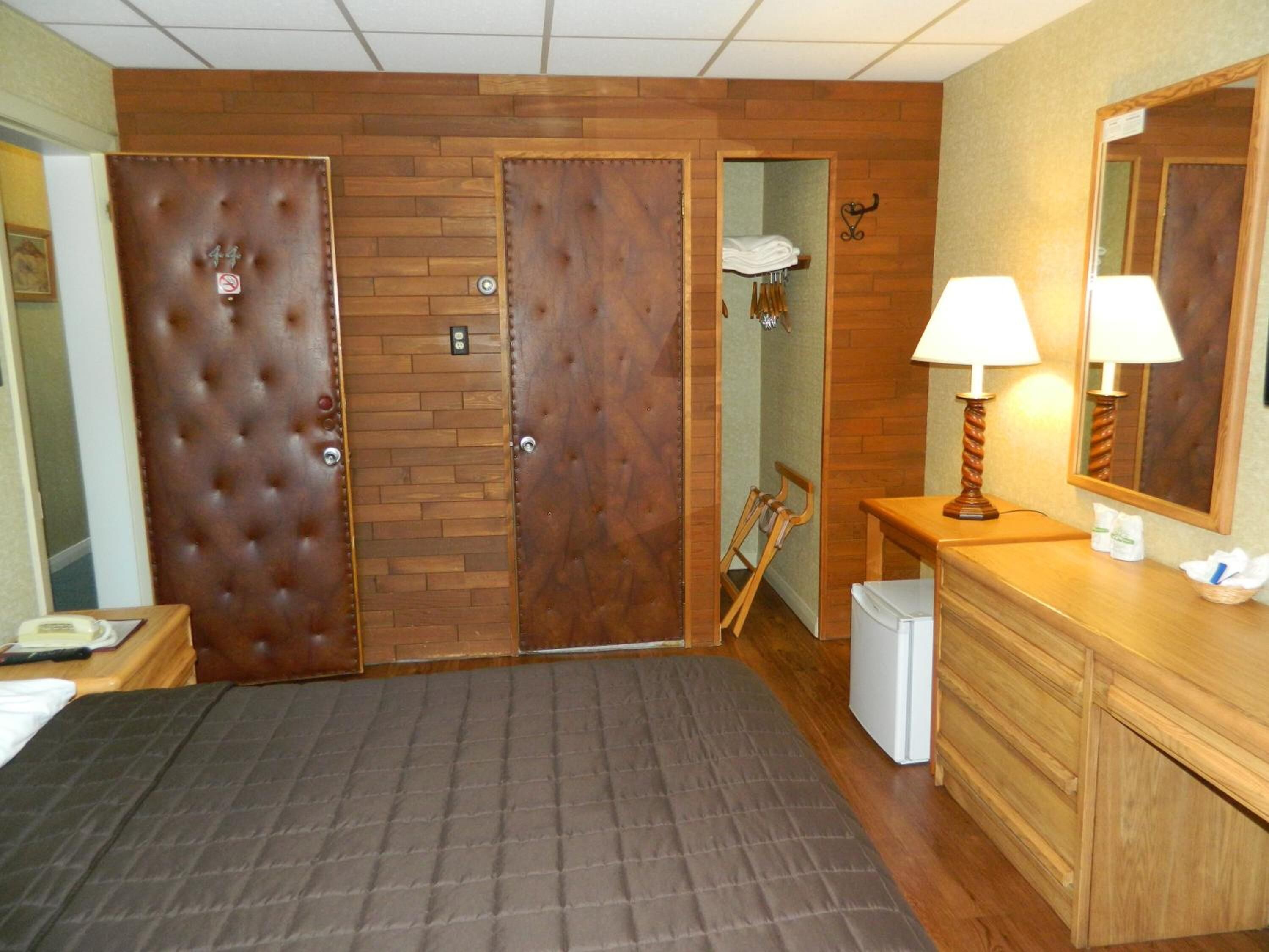 A hotel room with a large bed, a wooden wardrobe, a small desk with a lamp, and a mirror.