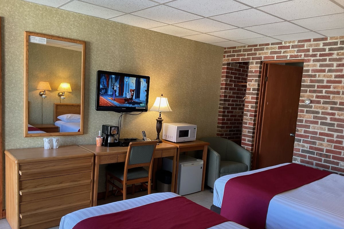 Hotellihuone, jossa on kaksi sänkyä, työpöytä tietokoneella, televisio, mikroaaltouuni ja pieni jääkaappi.