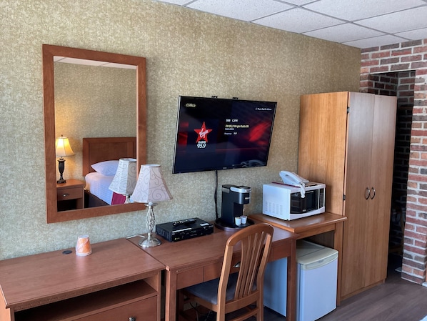 Habitación de hotel con escritorio de madera, un televisor mostrando Virgin Radio 95.9, un microondas, una cafetera y un armario.
