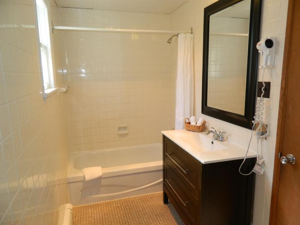 Une salle de bain avec une baignoire, un meuble-lavabo avec un miroir et un rideau de douche.