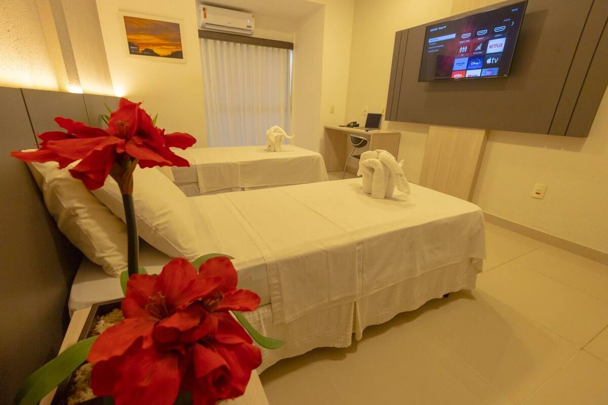 Une chambre d’hôtel avec deux lits, un téléviseur fixé au mur et une fenêtre avec des rideaux.