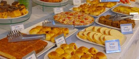 Un bufé con diferentes opciones de comida, incluyendo pasteles, bollos y pizza.