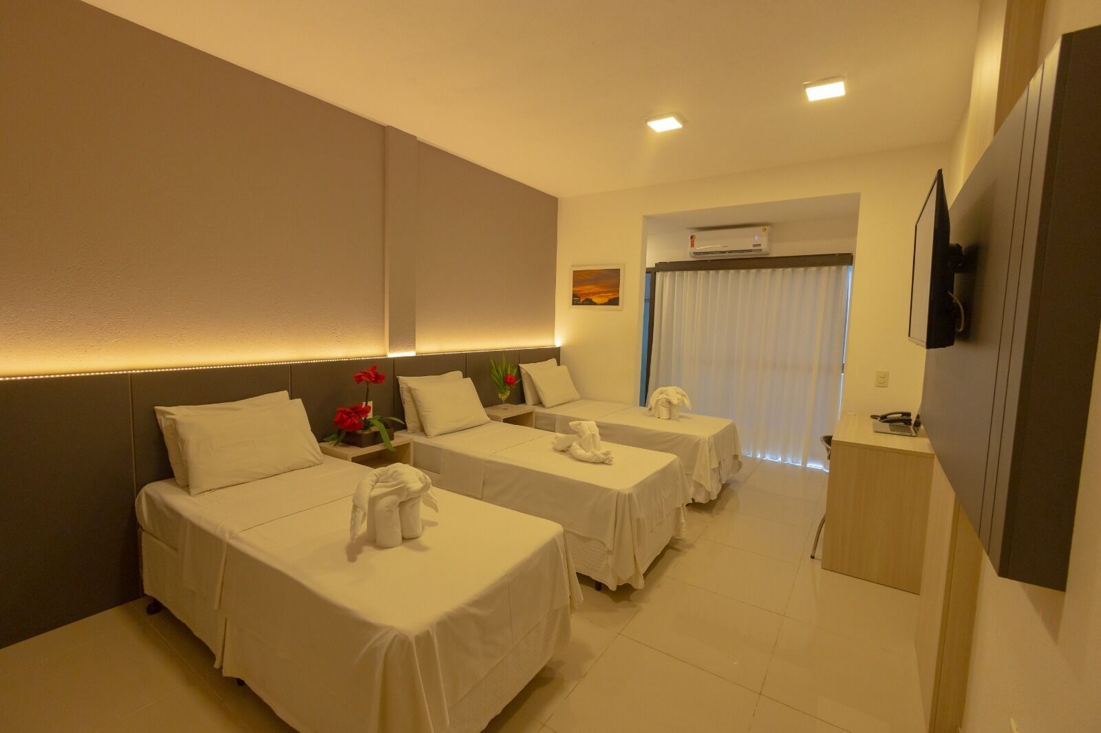 A hotel room with two single beds, a small desk, a TV, and an air conditioning unit.