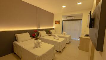 A hotel room with two single beds, a small desk, a TV, and an air conditioning unit.