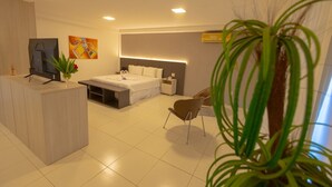 Habitació d'hotel moderna amb llit, taulell de nit, cadira, escriptori, televisió i obra d'art.