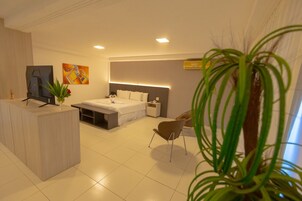 Quarto de hotel moderno com cama, mesa de cabeceira, cadeira, escrivaninha, televisão e obras de arte.