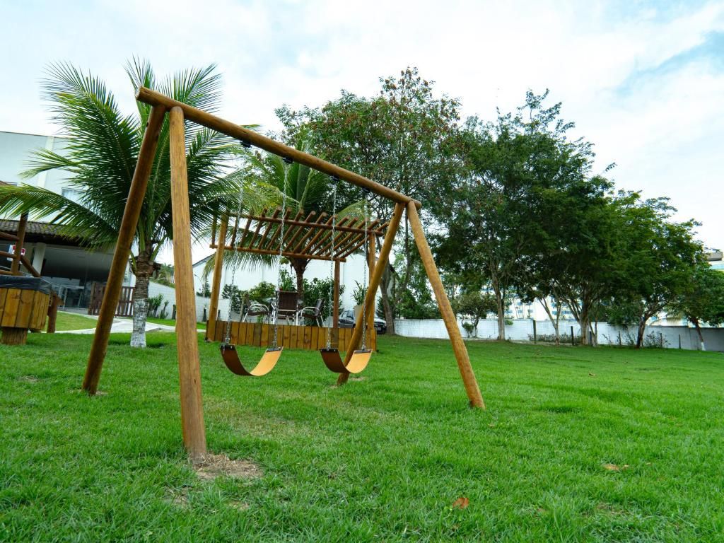 Un columpio de madera en un césped con árboles y un edificio al fondo.