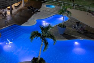 Uma piscina com um design ondulado singular, rodeada por espreguiçadeiras e palmeiras.