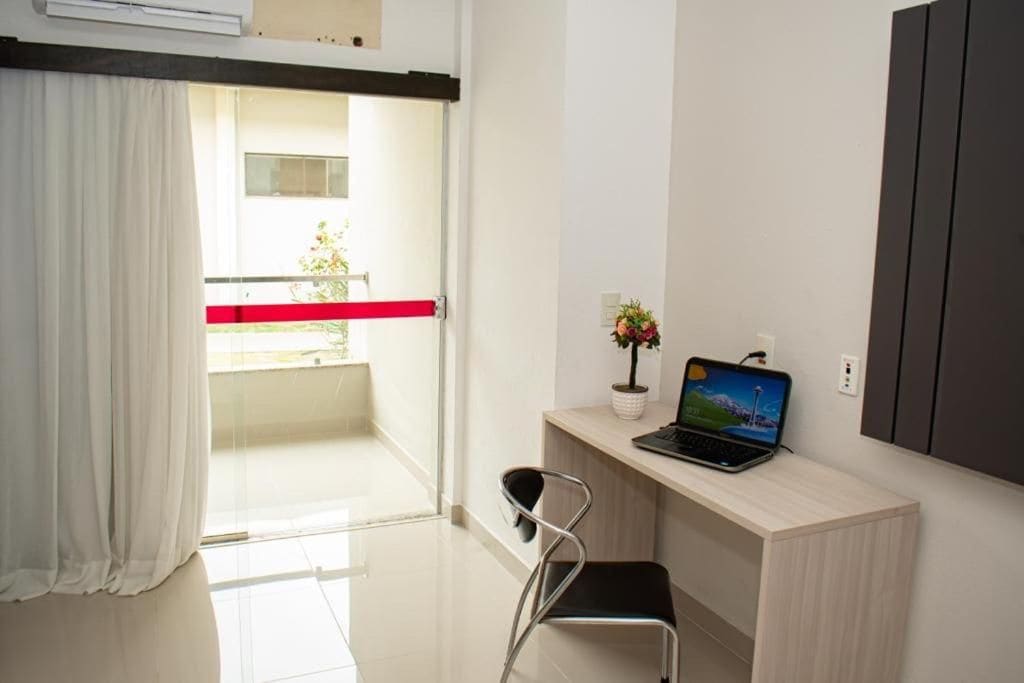 A modern room with a laptop on a desk, a chair, a window with curtains, and a balcony with a railing.