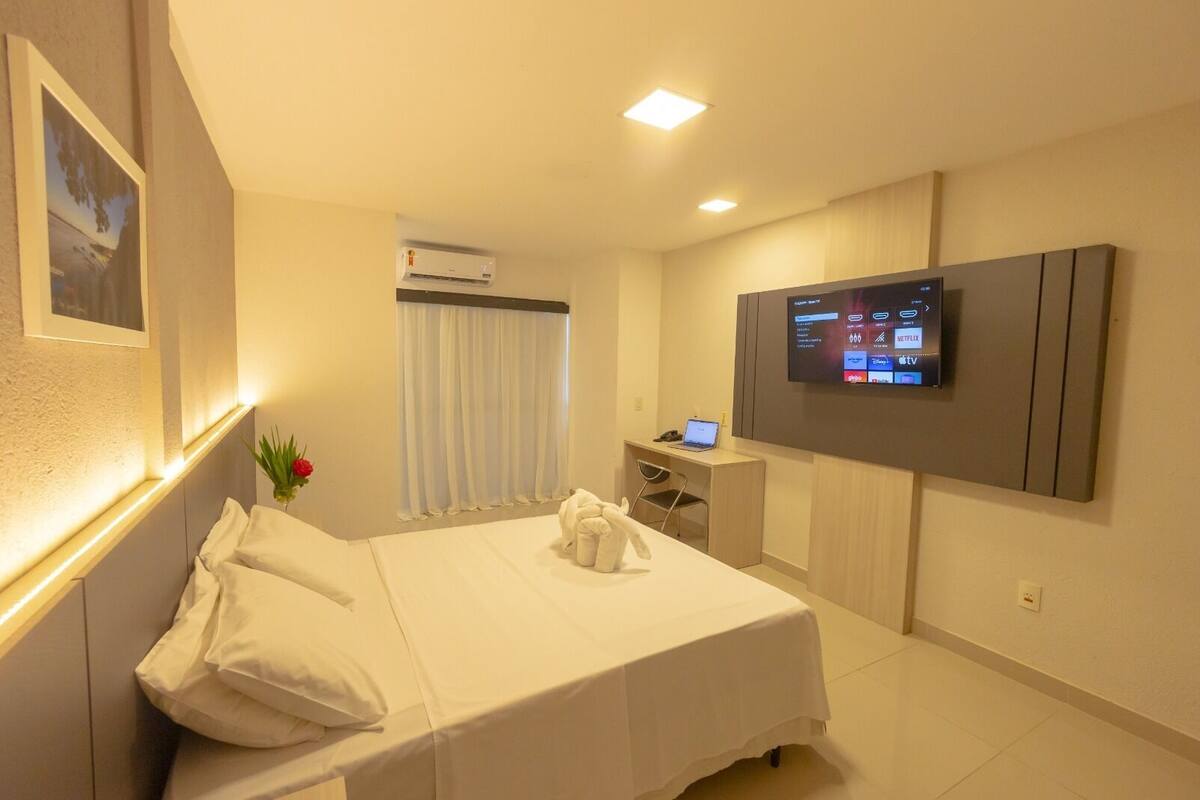 Une chambre d’hôtel équipée d’un lit, d’un bureau avec un ordinateur portable, d’un téléviseur fixé au mur et d’un appareil de climatisation.