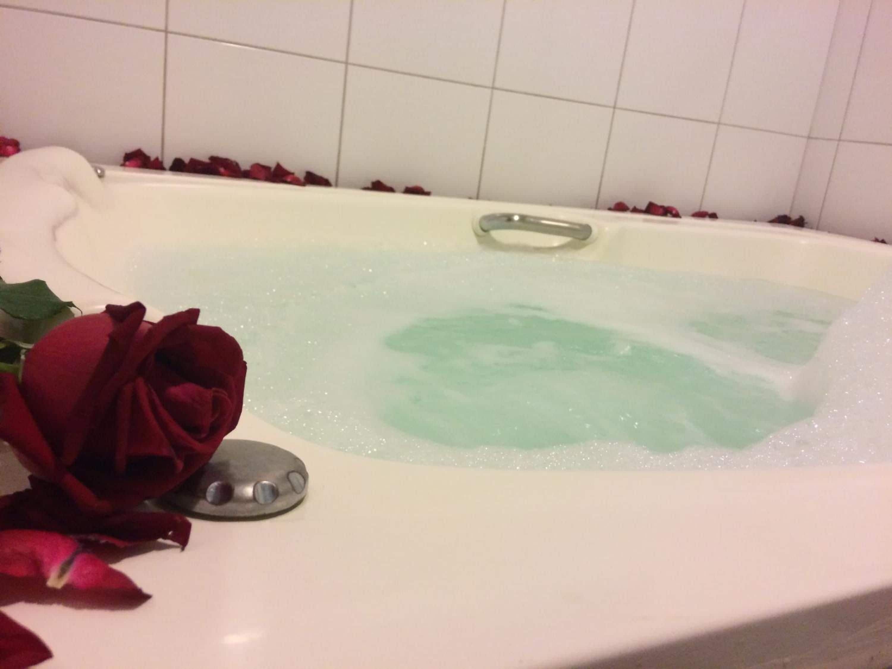 Ett badkar fyllt med rosenblad och en ros.