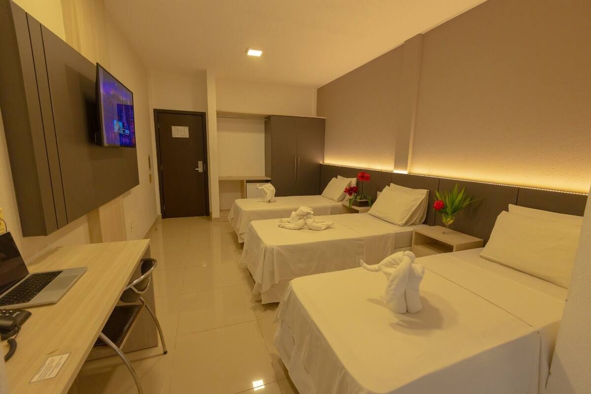 Une chambre d’hôtel avec deux lits, un bureau avec un ordinateur portable, une télévision et une porte donnant sur une salle de bain.