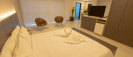 A hotel room with a neatly made bed, two brown chairs, a TV, and a cabinet.