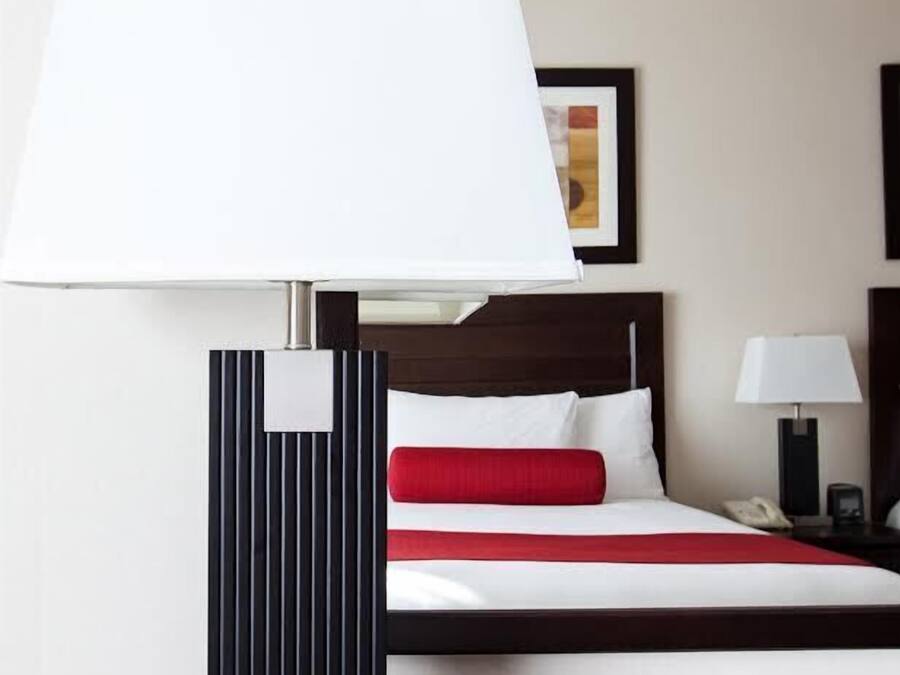 A hotel room with a bed, a bedside table with a lamp, and a wall-mounted picture.