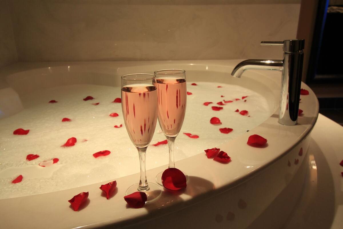 A bathtub with rose petals and two champagne glasses.