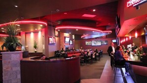 Un restaurante moderno con una barra curva, varias zonas de estar y un letrero de neón rojo.