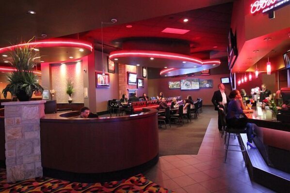 Un restaurante moderno con una barra curva, varias zonas de estar y un letrero de neón rojo.