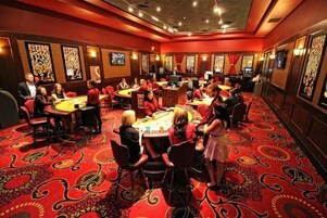 Un salón de casino con múltiples mesas de blackjack, piso de alfombra roja y cuadros en las paredes.