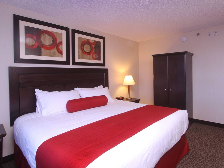 Una habitación de hotel con una cama grande, una mesita de noche, una lámpara y dos cuadros abstractos enmarcados en la pared.