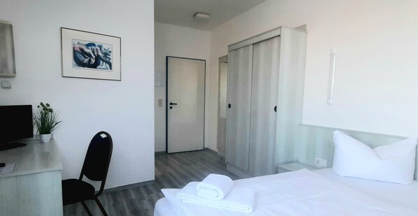 Habitación de hotel con una cama, un escritorio con computadora, una silla y una puerta que da a otra habitación.