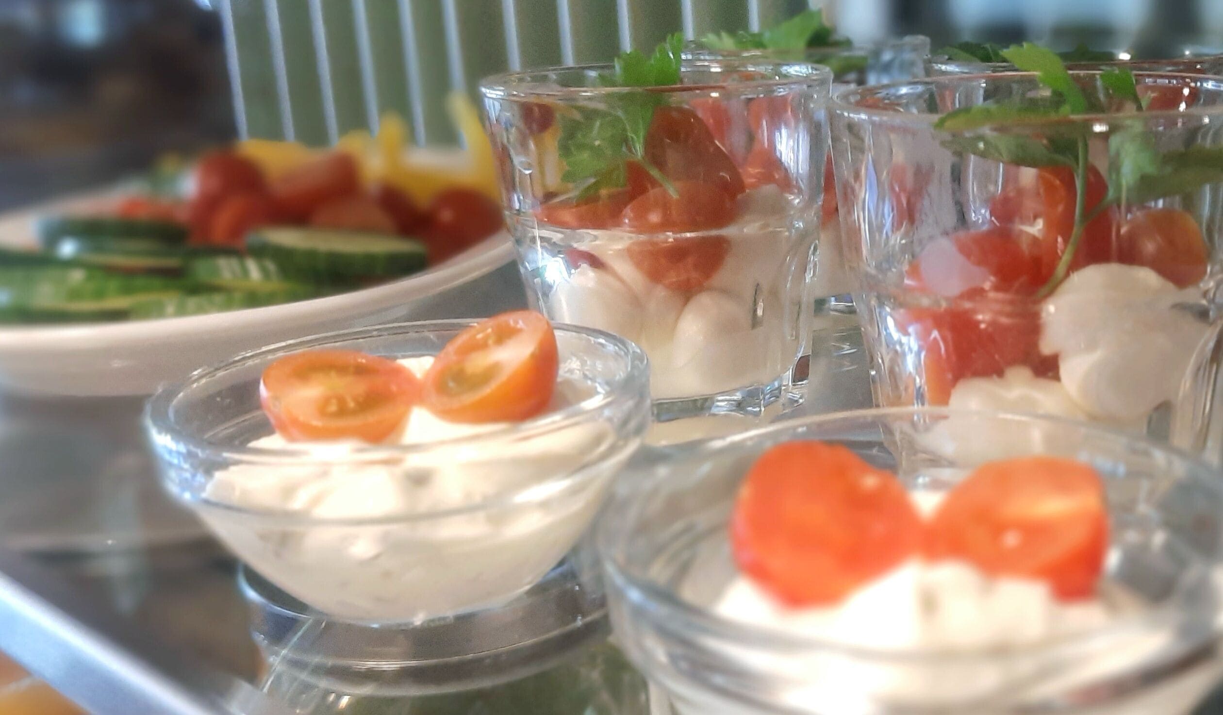 A tray with various food items including bowls of creamy substance with tomato slices, a plate with sliced vegetables, and a glass with a red substance.