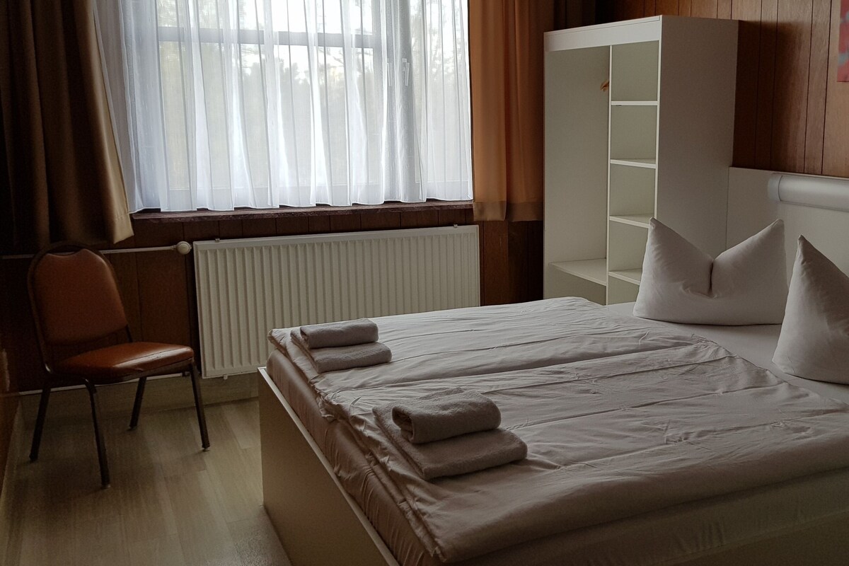 Una habitación de hotel con cama, una silla, un radiador y una ventana con cortinas.