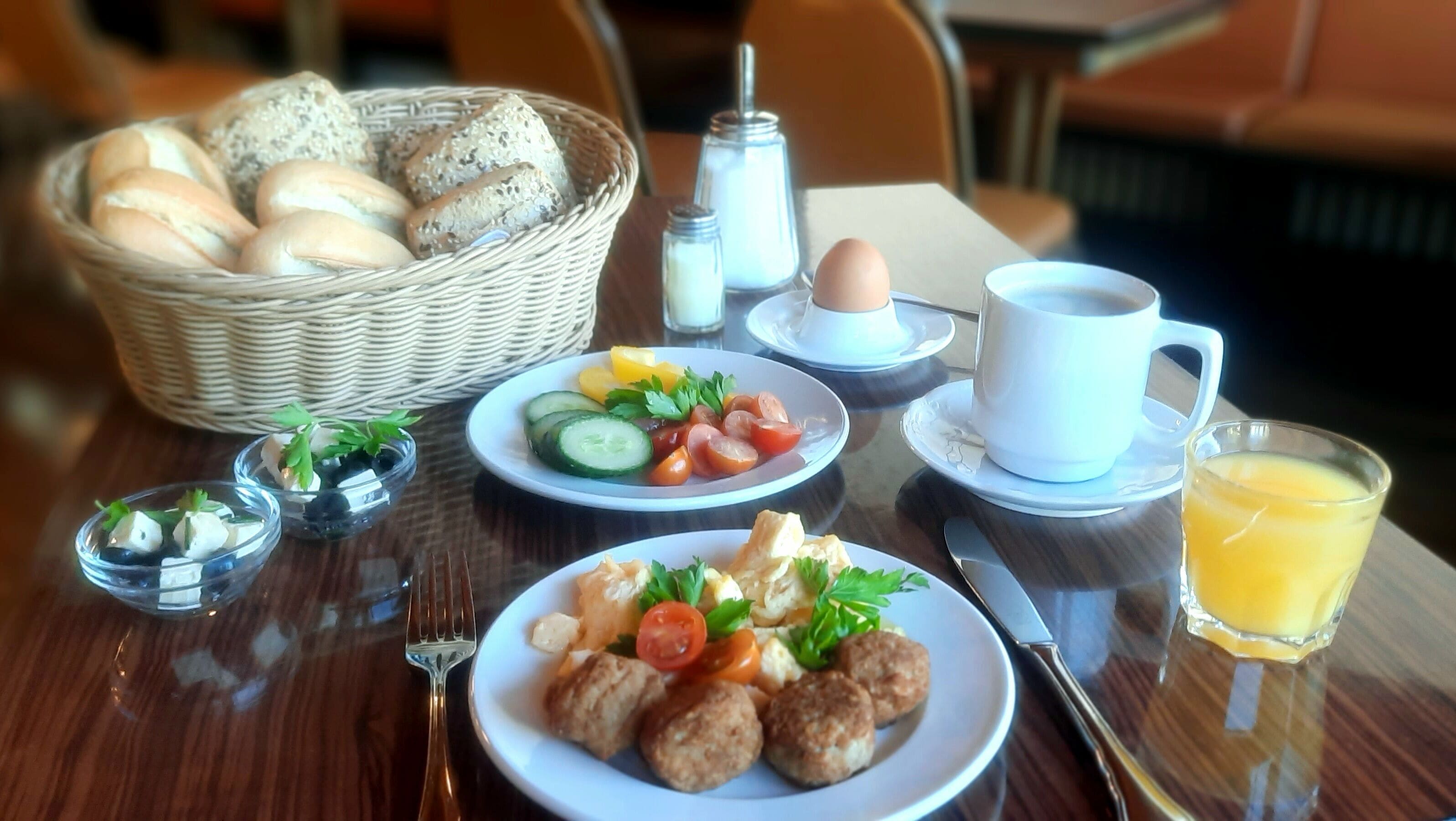 A breakfast setting with bread, eggs, a salad, and a glass of orange juice on a wooden table.