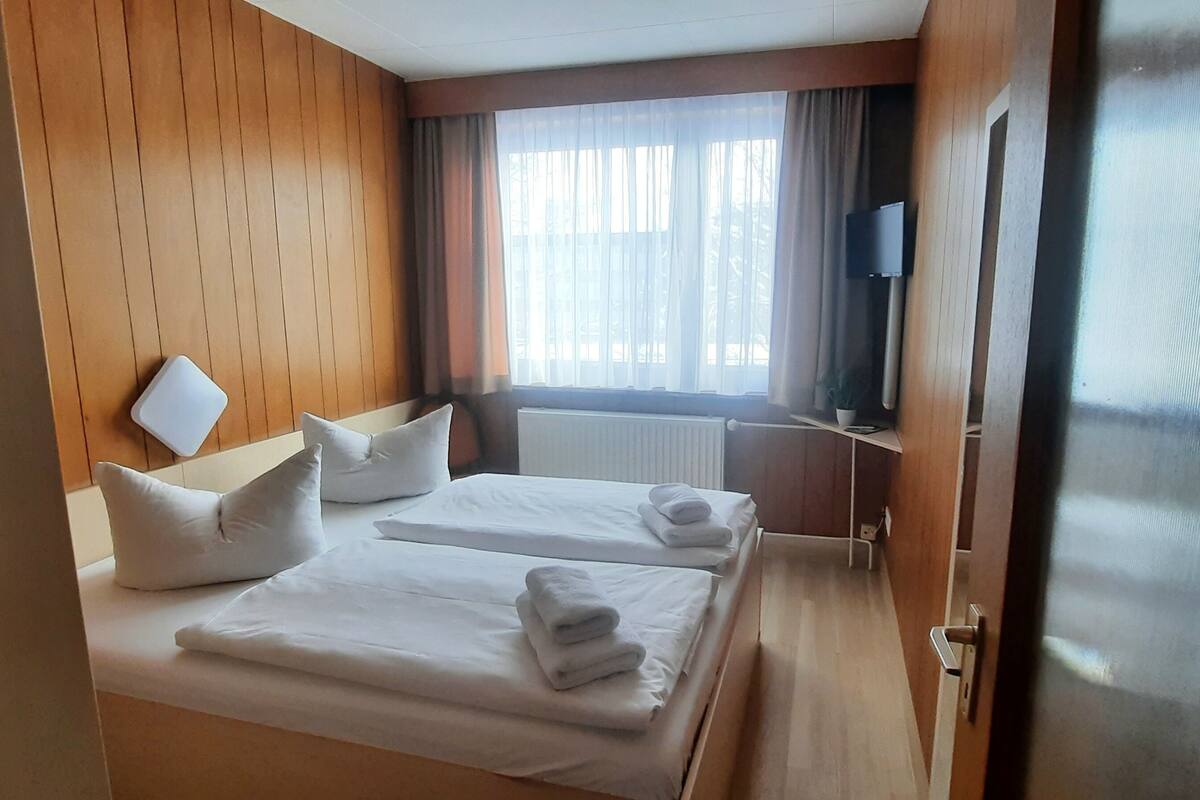 Ein Hotelzimmer mit zwei Betten, einem Fernseher, einem Fenster mit Vorhängen und einer Holzwand.