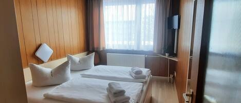 A hotel room with two beds, a TV, a window with curtains, and a wooden wall.