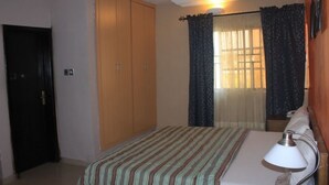 Een slaapkamer met een bed, nachtkastje, lamp, garderobe en een raam met gordijnen.