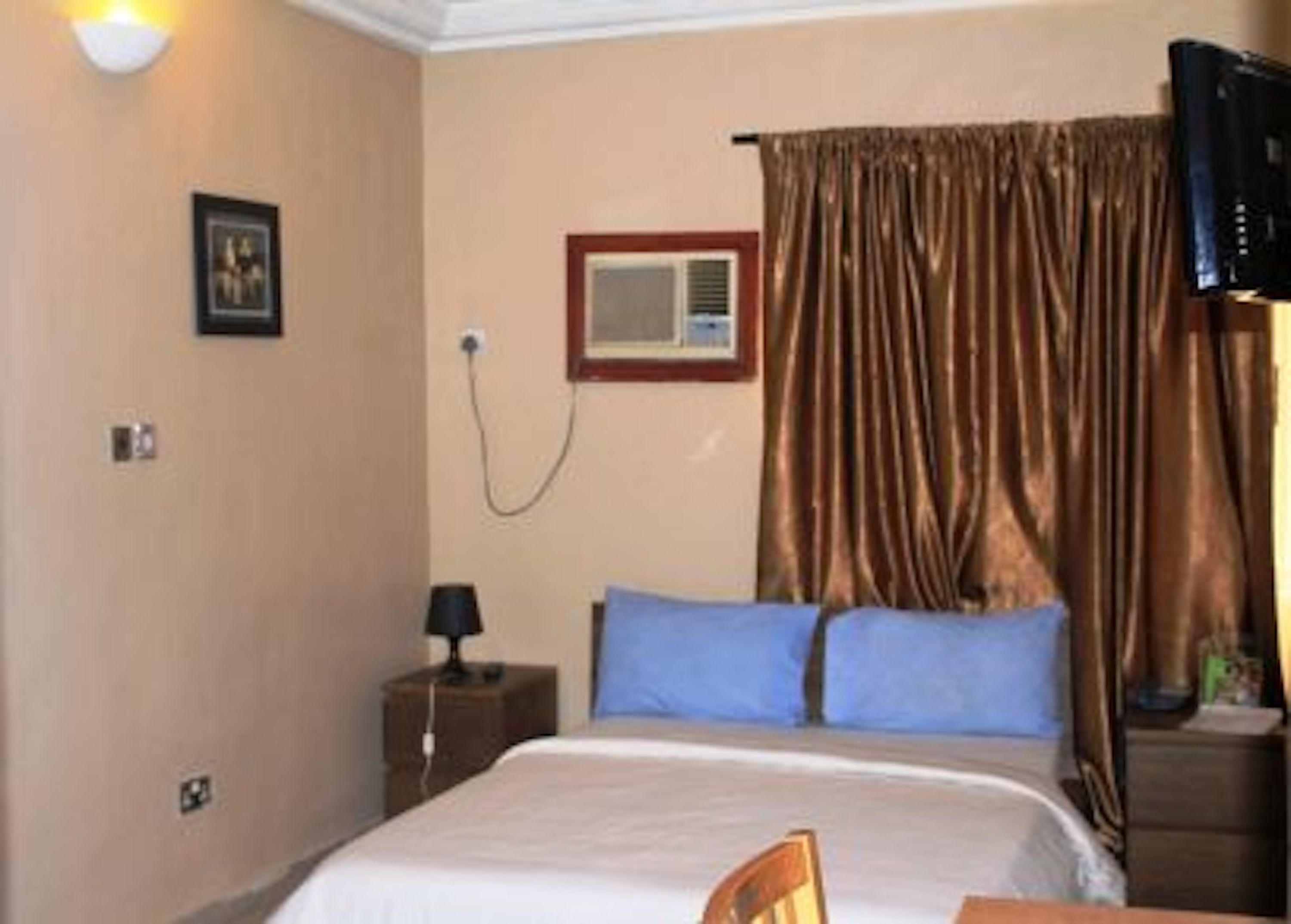 A hotel room with a bed, a nightstand, a lamp, a television, and a window with curtains.