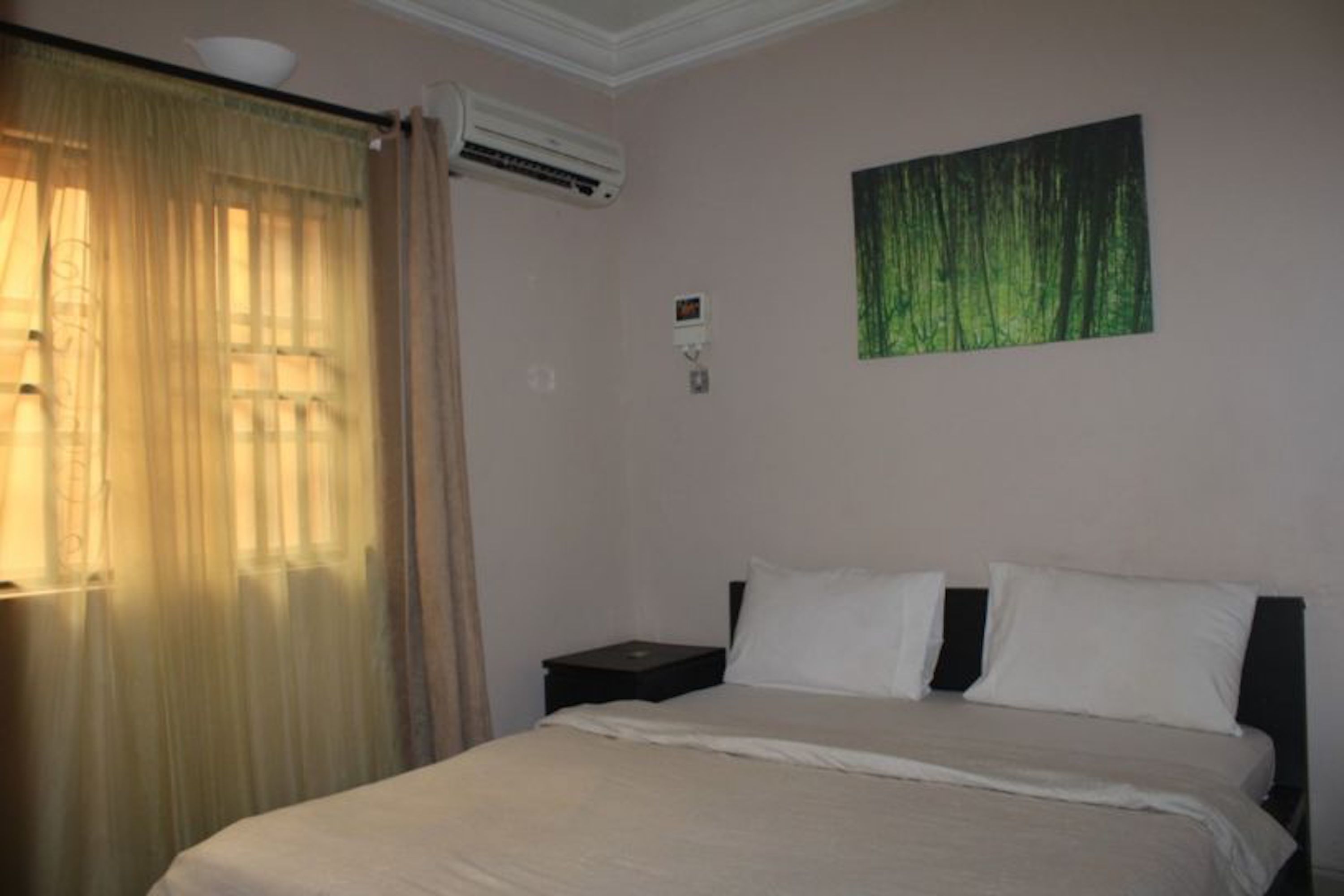 A bedroom with a bed, a nightstand, an air conditioning unit, and a window with curtains.