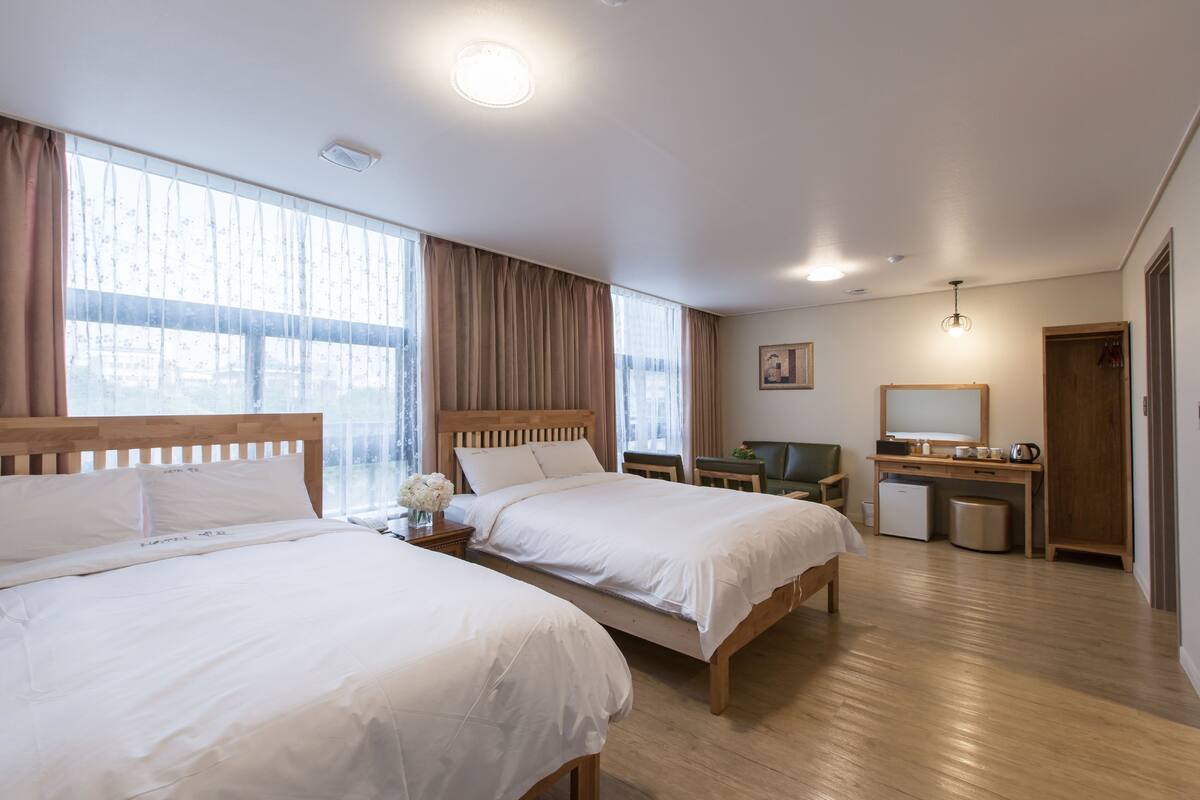 Une chambre d’hôtel avec deux lits, un bureau, une chaise, une petite poubelle et un miroir.