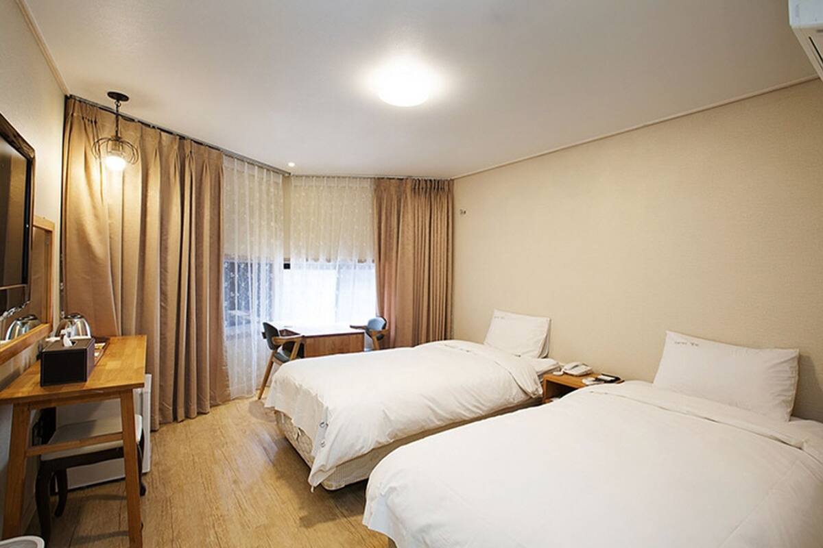 Une chambre d’hôtel avec deux lits, un bureau avec une chaise, une petite table et une fenêtre avec des rideaux.