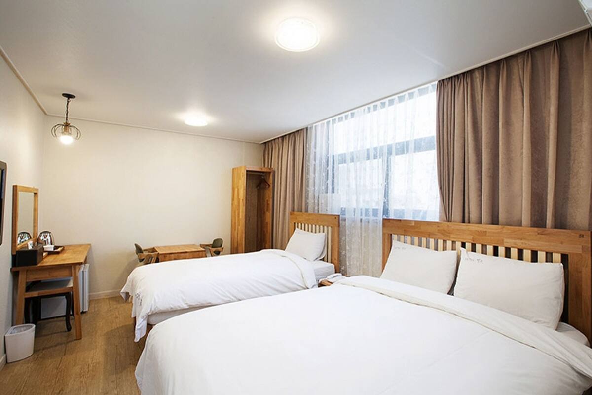 Une chambre d’hôtel avec deux lits, un bureau, une chaise, une petite table et une fenêtre avec des rideaux.