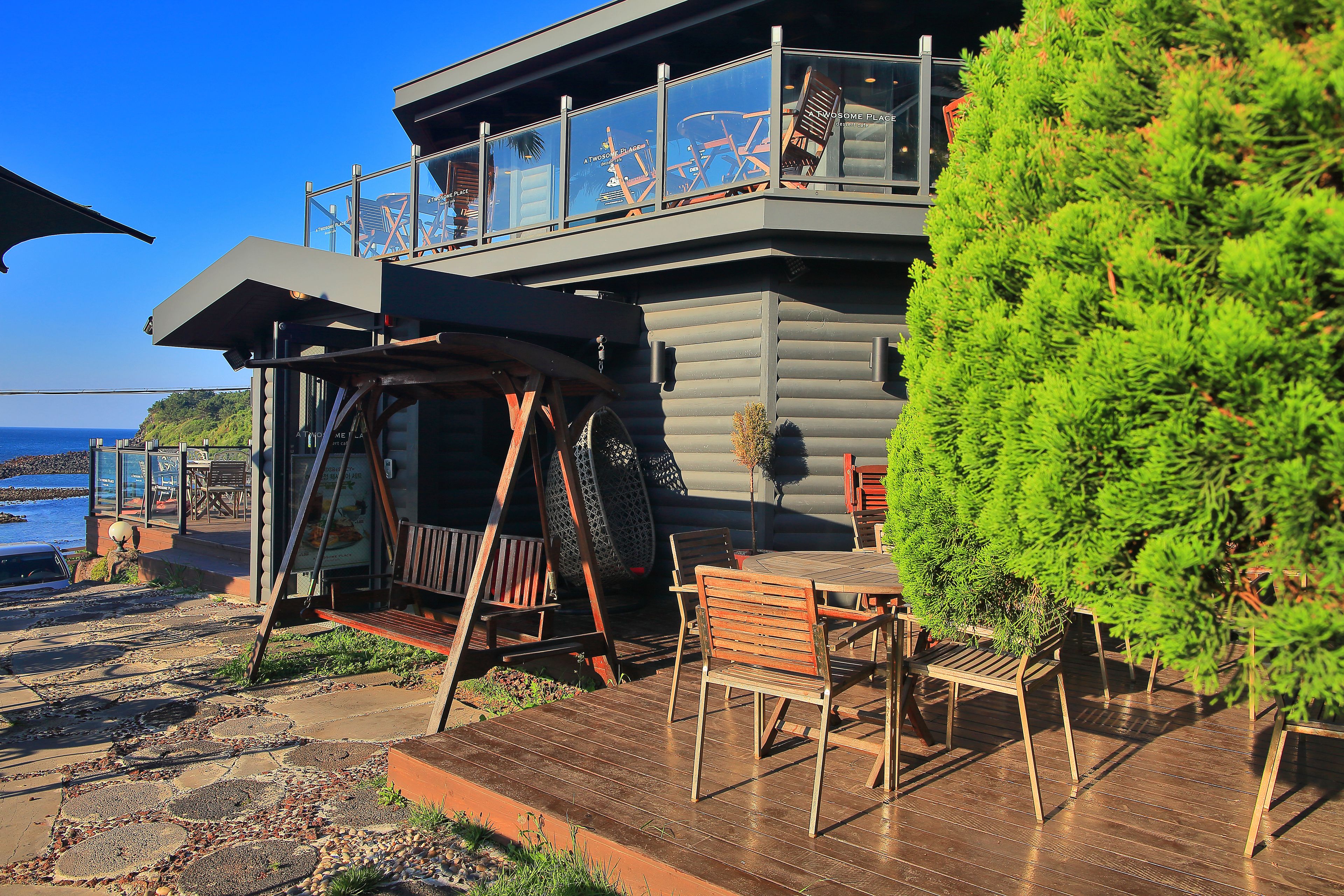 A log cabin with a balcony overlooking the sea, outdoor seating, and a wooden deck.