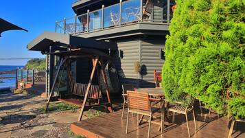 A log cabin with a balcony overlooking the sea, outdoor seating, and a wooden deck.