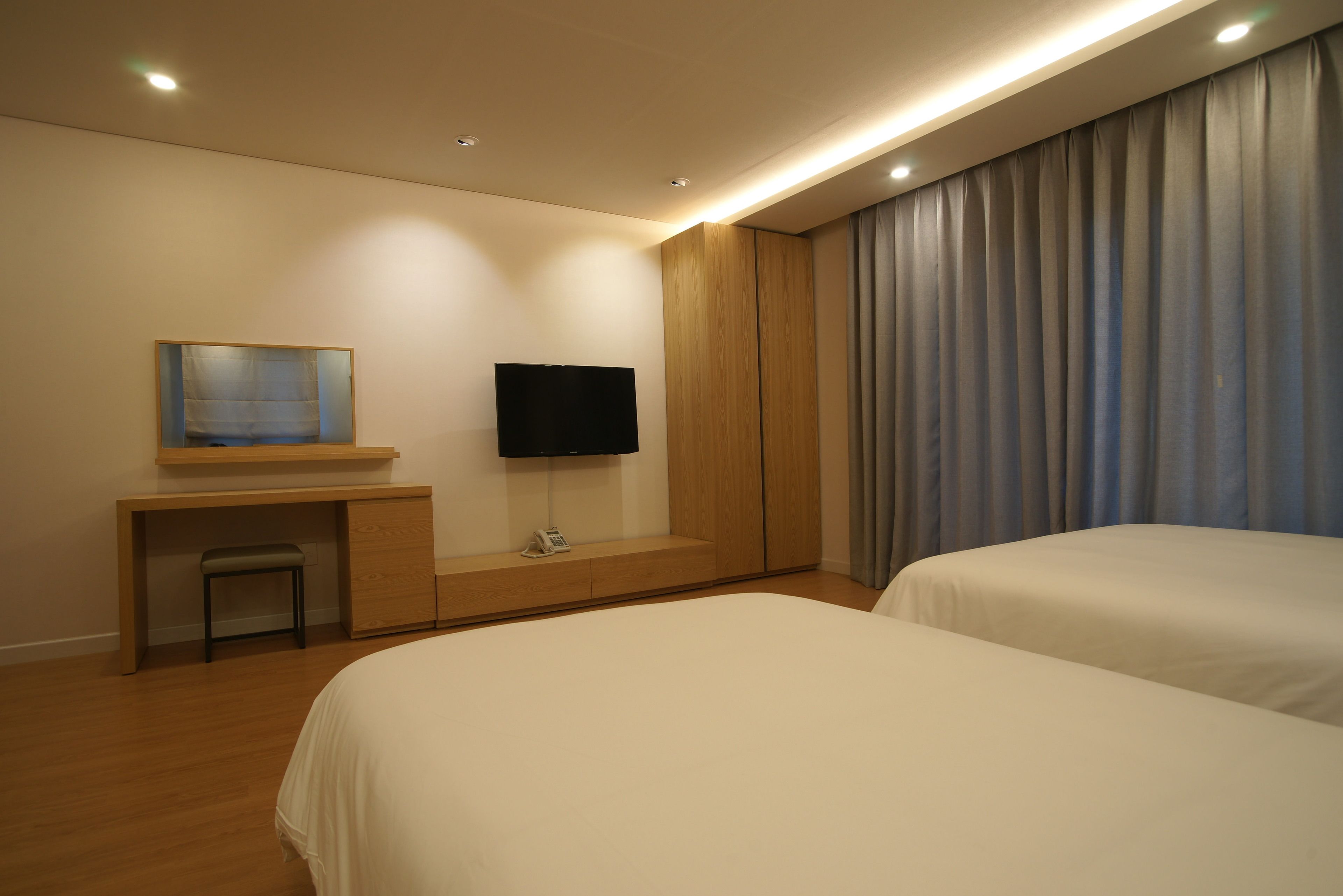 Une chambre d’hôtel avec deux lits, un bureau avec une chaise, un téléviseur à écran plat fixé au mur et une grande fenêtre avec des rideaux.