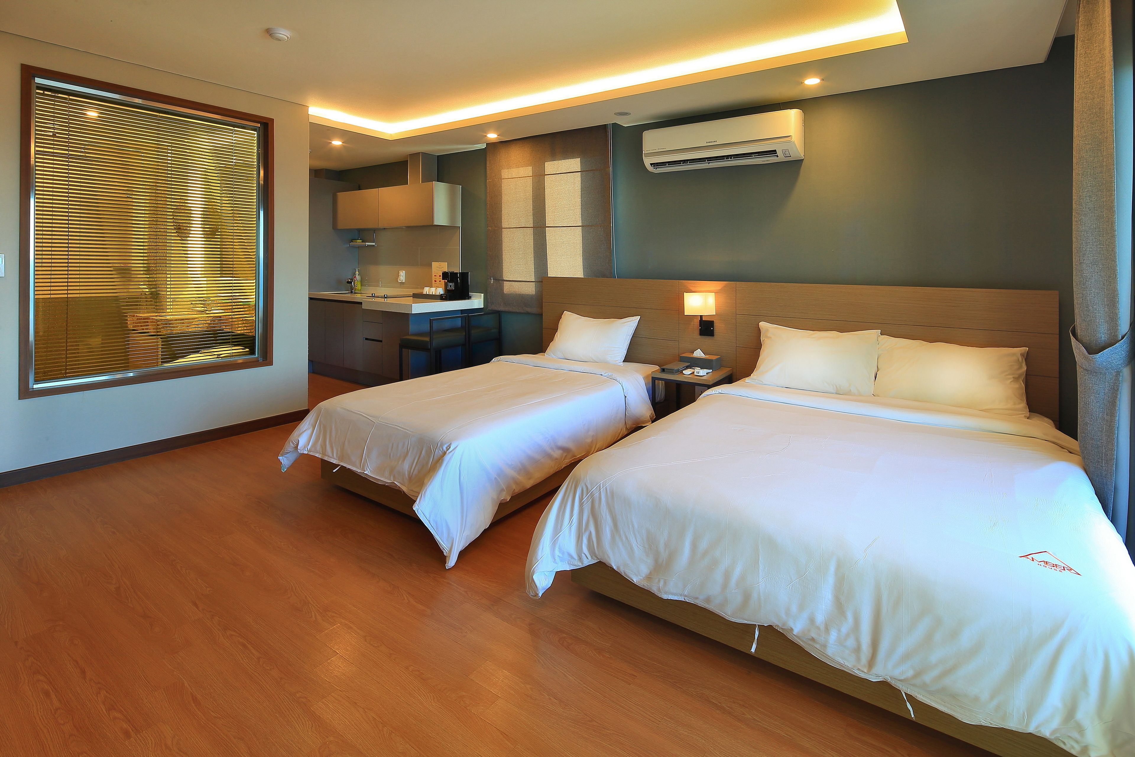 Habitación de hotel con dos camas, kitchenette y aire acondicionado.