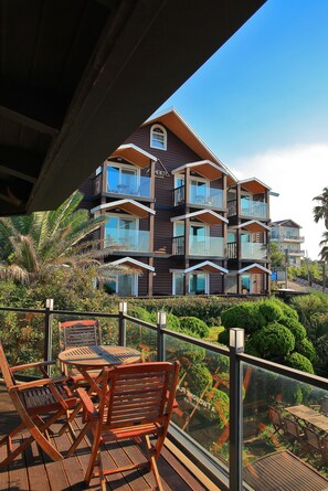 A multi-story wooden building with balconies and large windows, surrounded by lush greenery. - Amber House (Jeju City)