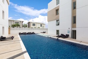 A modern pool area with lounge chairs and a clear blue pool, surrounded by white buildings with balconies. - The Regent Residence Kamala (Kamala)