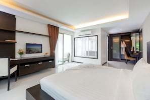 A modern hotel room with a large bed, a desk, and a chair. There is a window with blinds, a door leading to a balcony, and an air conditioning unit on the wall.