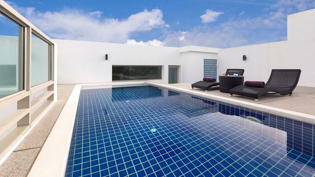 A modern indoor swimming pool with clear blue tiles, two lounge chairs, and a glass-enclosed area. - The Regent Residence Kamala (Kamala)