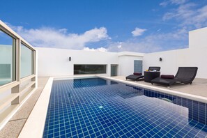 A modern indoor swimming pool with clear blue tiles, two lounge chairs, and a glass-enclosed area. - The Regent Residence Kamala (Kamala)