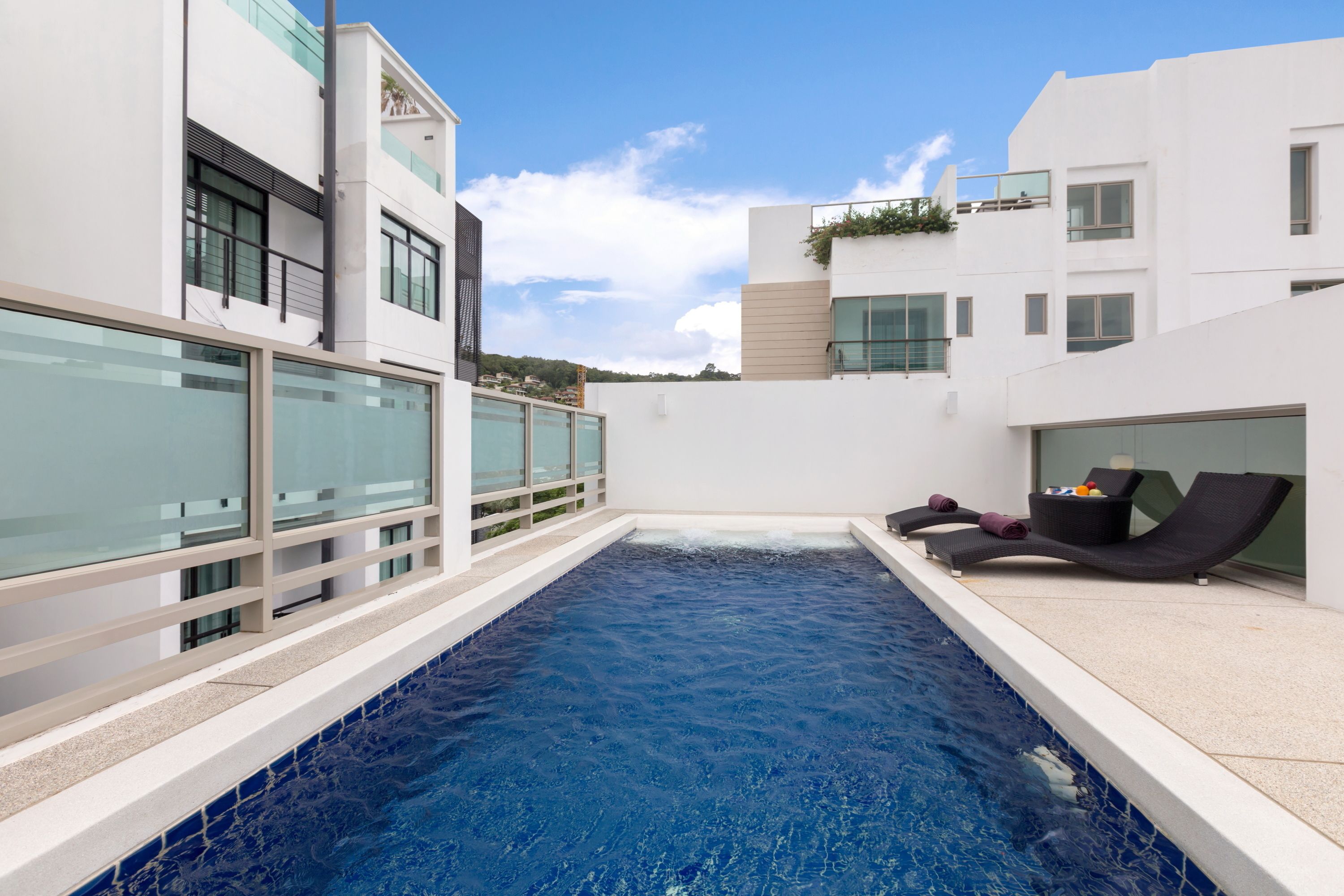 Un espace piscine moderne avec des rampes de protection en verre, des chaises longues et une piscine à l’eau d’un bleu cristallin.